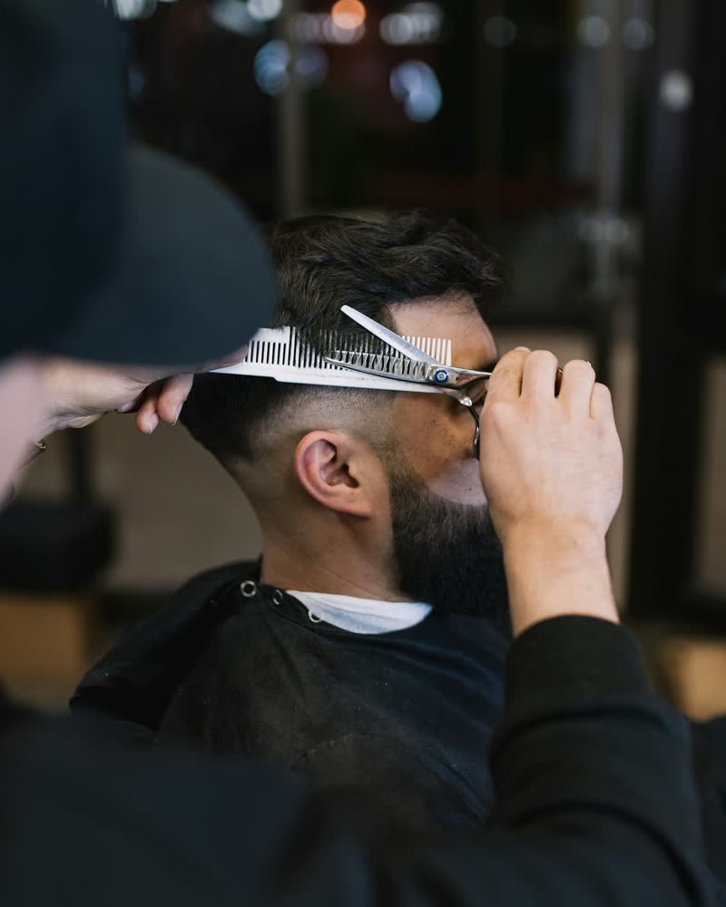 Barbeiro aparando o cabelo com pente e tesoura